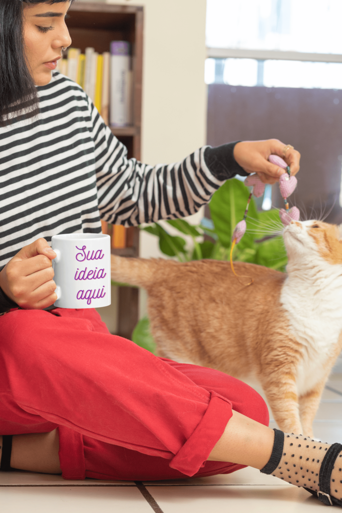 Moça brincando com um gato e segurando uma caneca personalizada